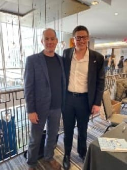 Two men stand together with a book on a table